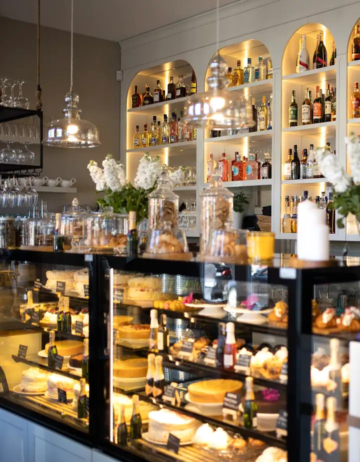 Białe łukowe półki z podświetleniem i witryna z ciastami w Elite Cafe